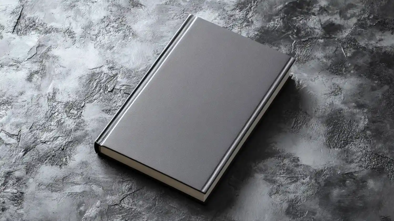 A closed, plain gray hardcover book rests on a textured gray and black surface. canadianghostwriters