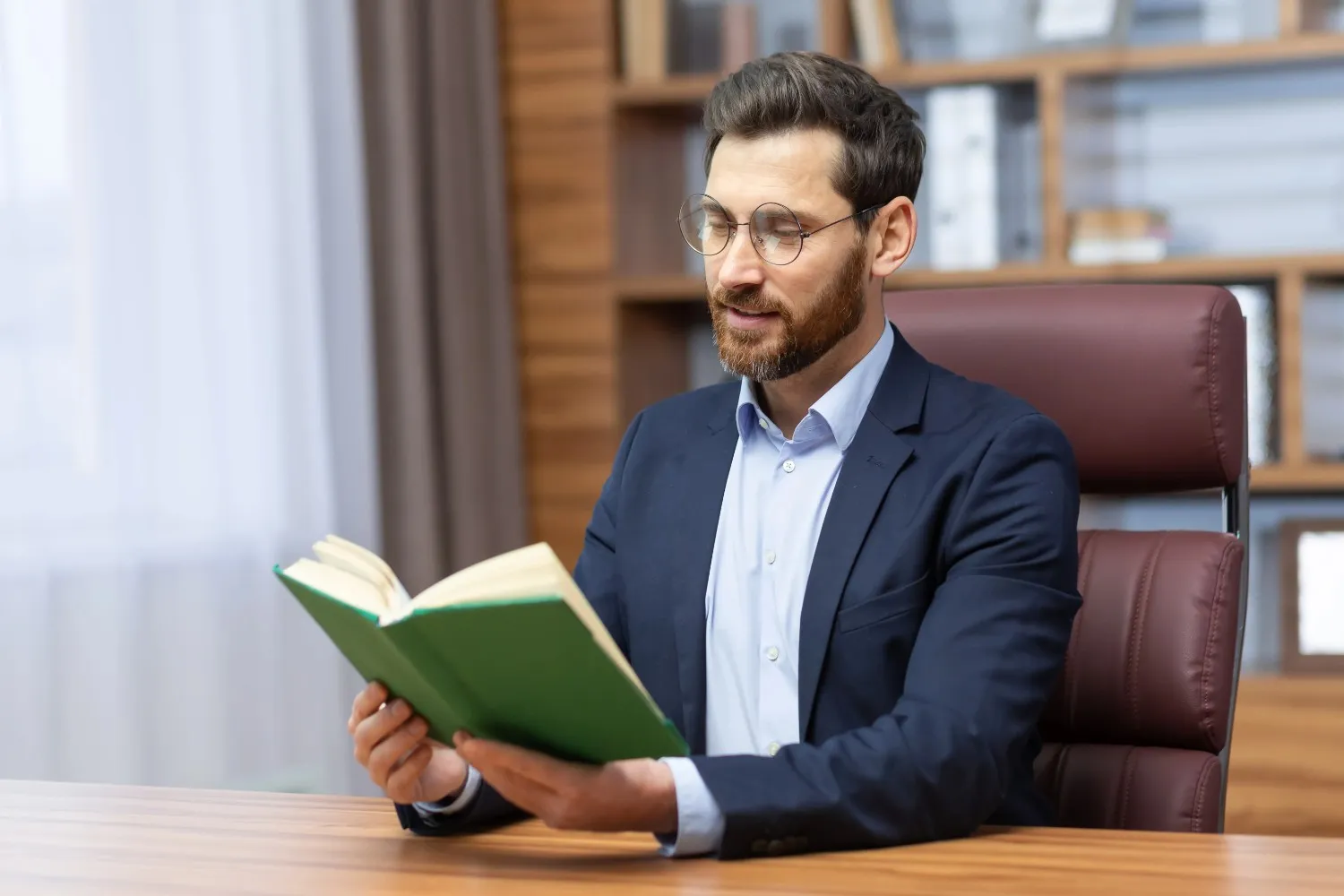 A man in a suit reading a book while sitting at a desk.canadianghostwriters