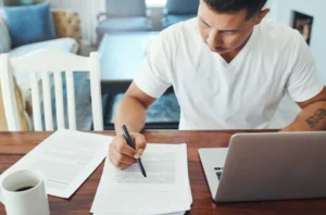 remote-work-laptop-man-with-documents-table-review-sentence-structure-editing-proofreading-freelance-person-check-grammar-verify-references-format-guidelines-home canadianghostwriters