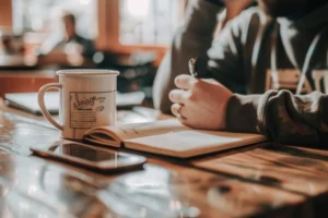 this-image-depicts-person-writing-brown-wooden-table-with-white-ceramic-mug-nearby-adding